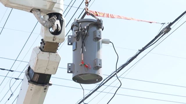 Installing a transformer onto a utility pole under a clear sky