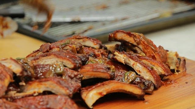 Drizzling sauce over deliciously grilled ribs on a wooden cutting board