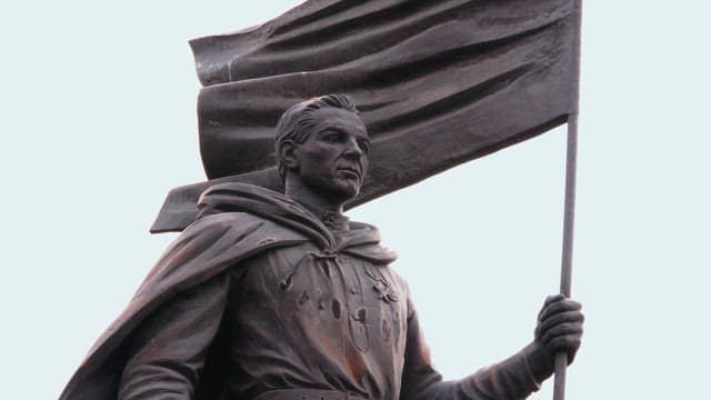 Historical statue of a man with a cloak under a cloudy sky