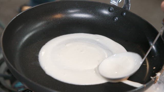 Putting a thin layer of flour batter in a frying pan