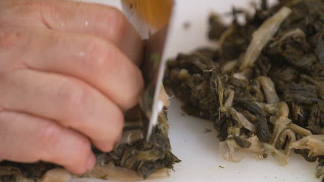 Cutting boiled dried radish greens with a knife on a cutting board