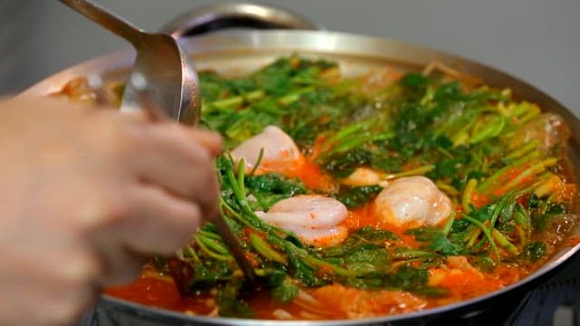 Ladleful of kimchi stew with puffer fish, vegetables and seafood