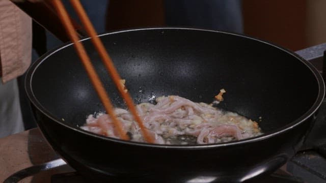 Stir-frying meat with chopsticks in a frying pan with oil