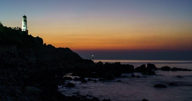 Ocean sunset with lighthouse and rocky shore
