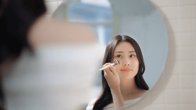 Woman applying makeup with a brush in front of a mirror