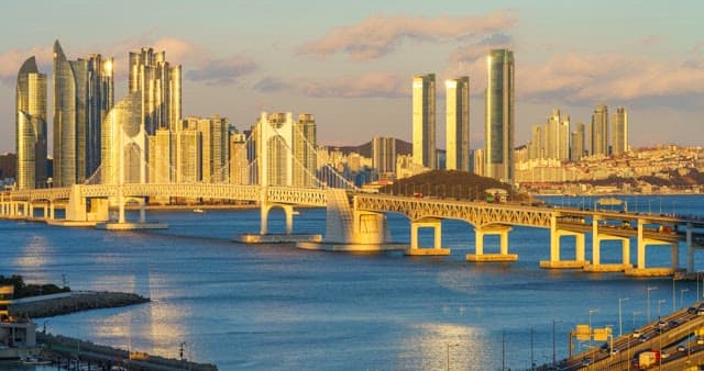 From evening to night view of a bustling port city Busan with tall skyscrapers and Gwangan Bridge