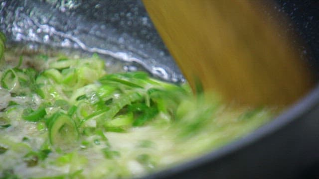 Green onions being sautéed in a pan