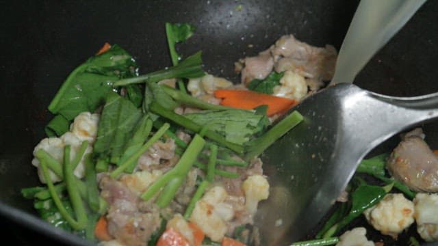 Pouring broth into a pan and stir-frying vegetables and meat