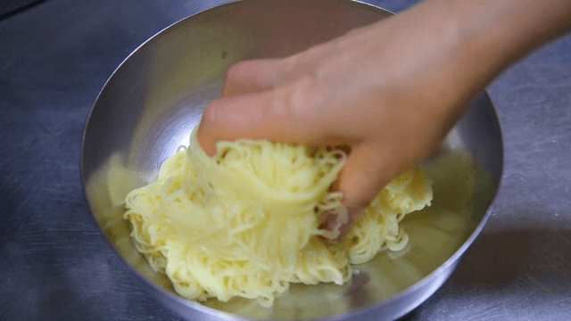 Noodles being placed in a metal bowl