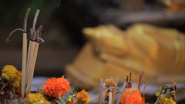 Incense and flowers near a golden Buddha statue