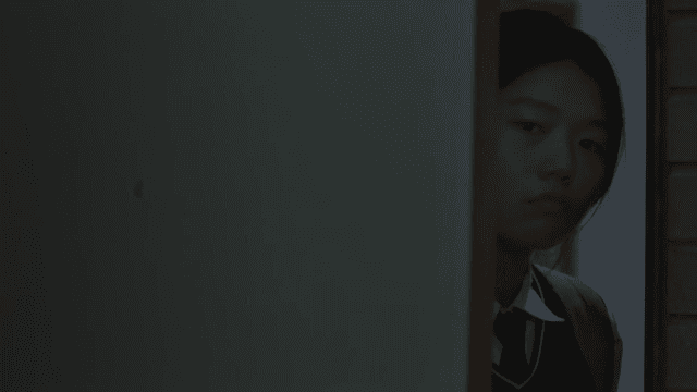 Female student in school uniform opens the door to a dark room