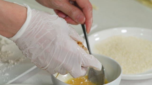 Hands preparing food with egg wash and breadcrumbs