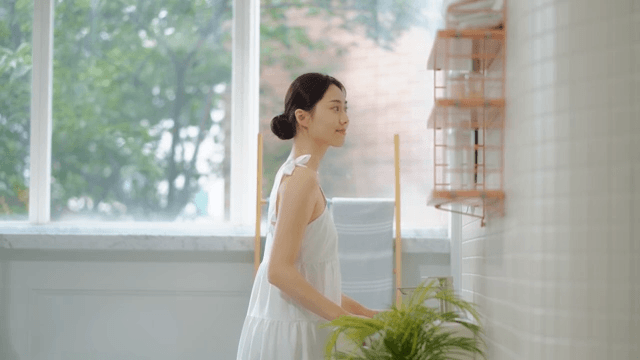 Woman in white clothes smiling and touching her face in a bright room