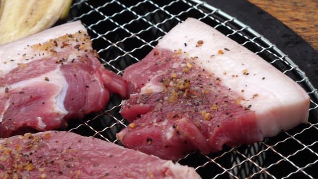 Grilling seasoned pork belly slices on a barbecue grill