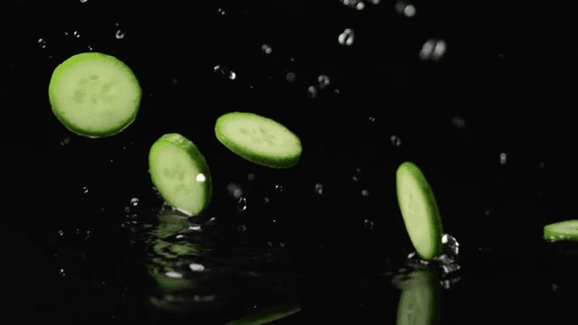 Slices of cucumber falling on water on black background