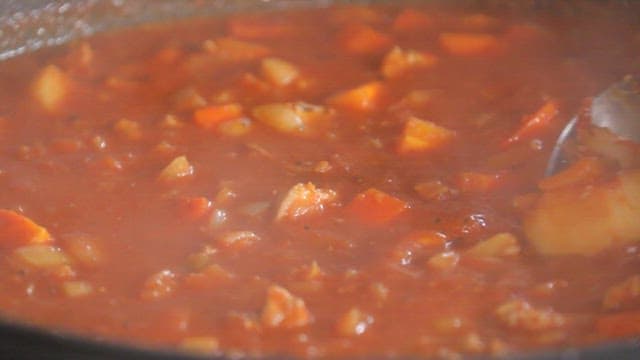Stirring the stew with tomatoes and pork with a ladle