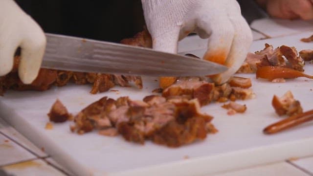 Cutting cooked pig trotters with a cleaver on a cutting board