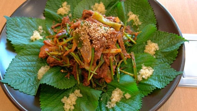 Spicy seasoned meat with perilla leaves on a plate on a wooden table
