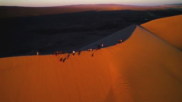 People with Sunset Over Desert Dunes