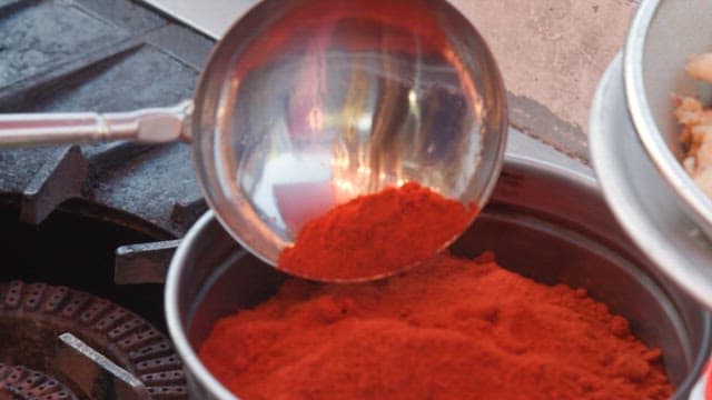 Chef cooking vegetables with red pepper powder in a hot pan