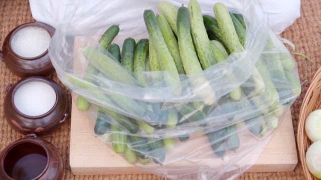 Fresh cucumbers in plastic wrap prepared on a wooden cutting board