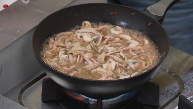 Adding chili peppers to the sizzling meat in the frying pan