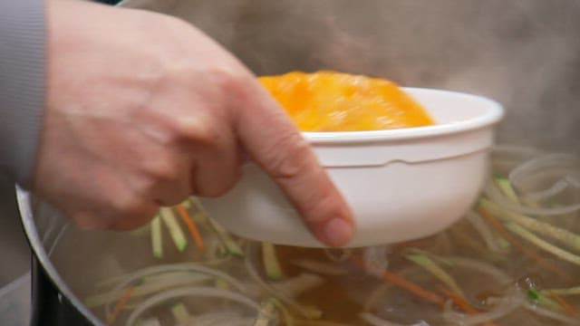 Pouring egg mixture into warm vegetable broth in a pot
