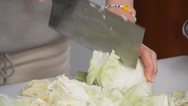Cutting fresh cabbage with a knife on a cutting board in the kitchen