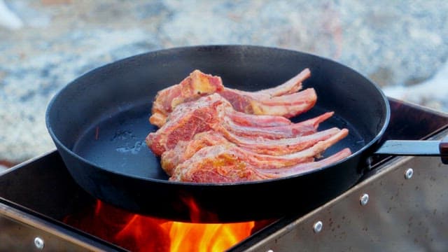 Fresh lamb being cooked in a frying pan on the portable stove