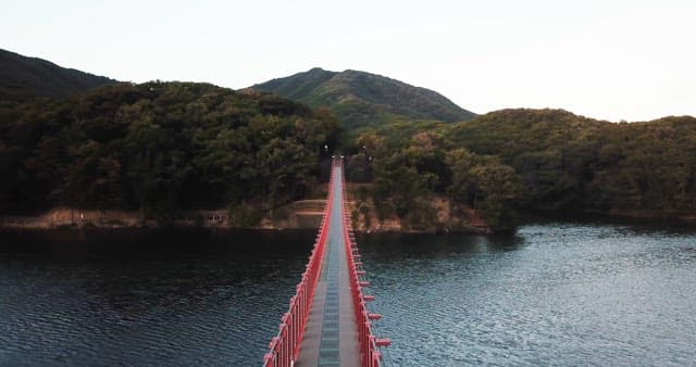 Red suspension bridge over a calm lake