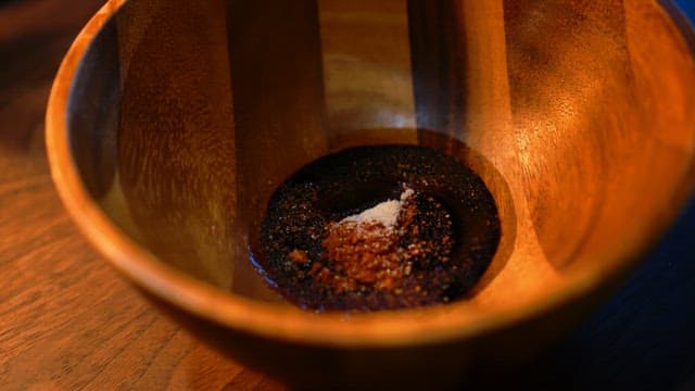 Preparing a wooden bowl with soy sauce, chili flakes, and salt