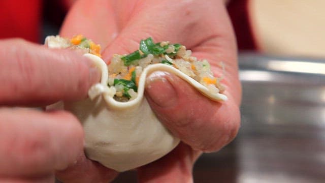 Hands making dumplings with filling