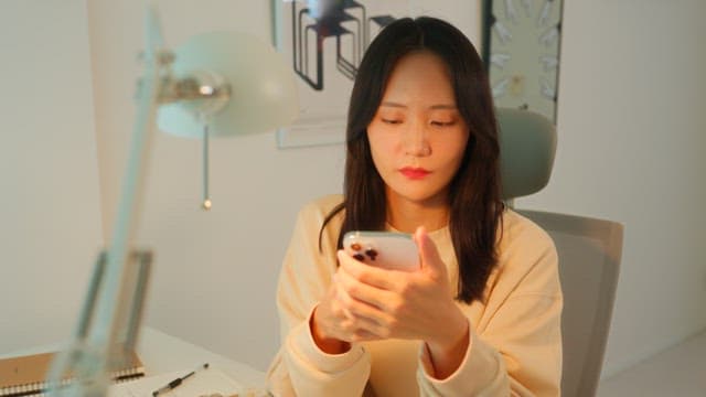 Woman using a smartphone at a desk in a calmly lit room