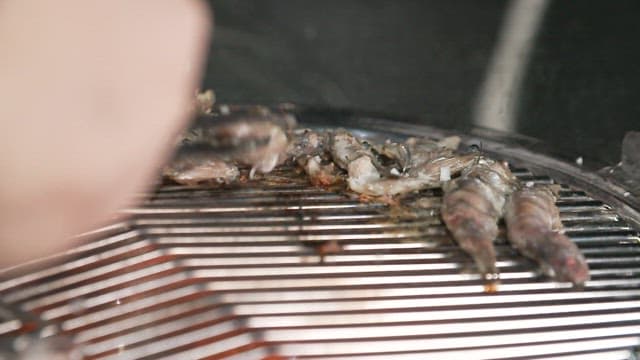 Grilling anchovies on a grill using tongs