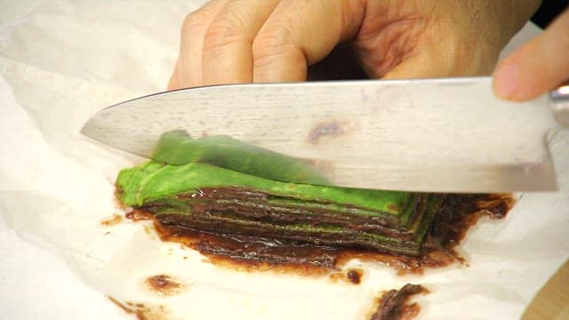 Slicing the chocolate-covered spinach crepe cake with a knife