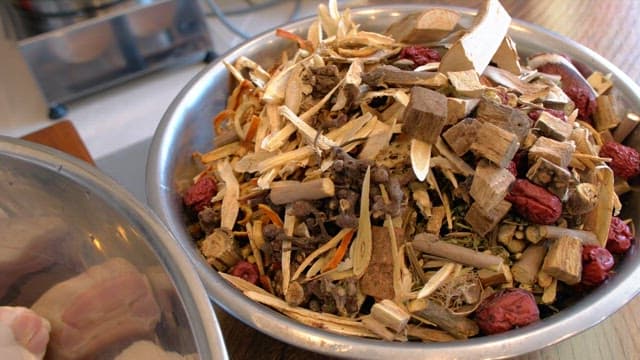 Various dried herbs and roots in a metal bowl