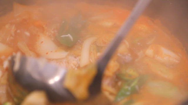 Scooping up spicy stew boiling in a pot with a ladle