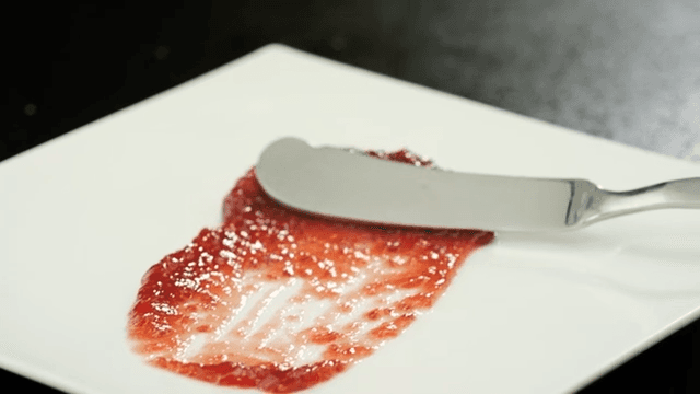 Spreading strawberry jam with a butter knife on a white plate