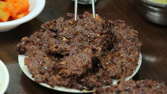 Plate of glossy tteokgalbi on a table with side dishes