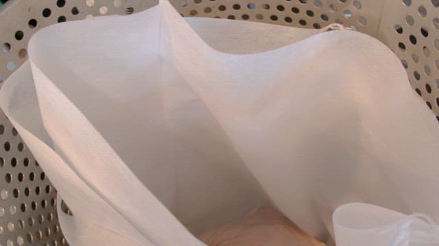 Raw meat being placed in a fabric strainer inside a metal container