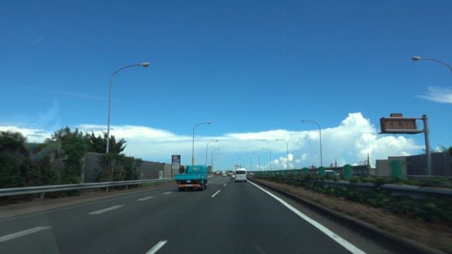 Cars on a highway with clear sky and fluffy clouds