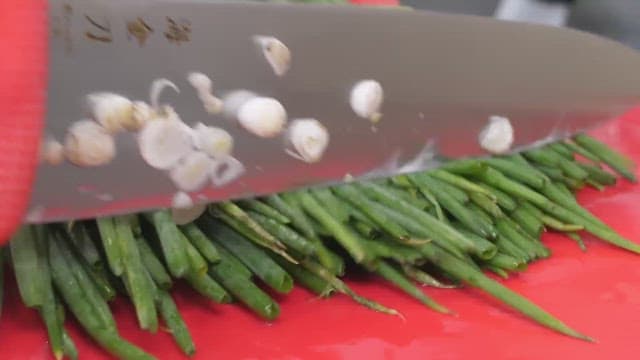 Fresh green onions being finely chopped with a sharp knife.