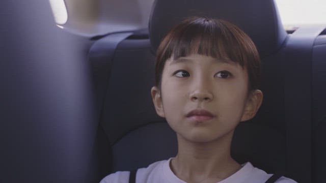 Young girl seated in a car, looking thoughtful.