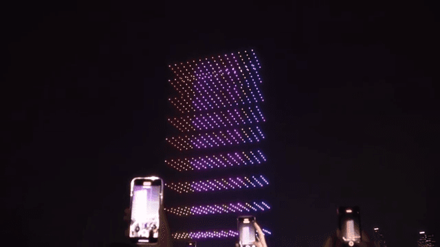People filming a nighttime drone light show by the river