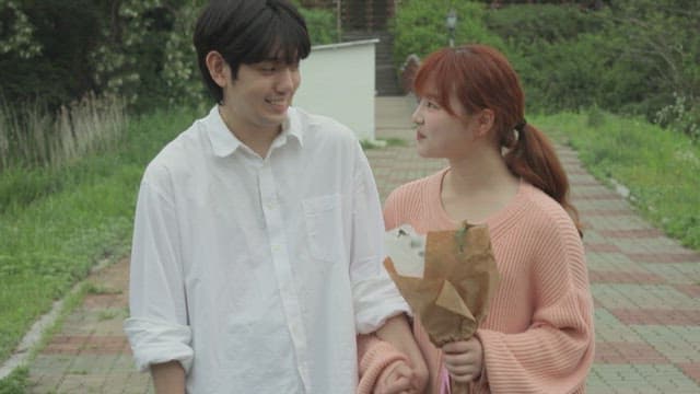 Young couple walking in a park on a cloudy day, looking happy and holding hands