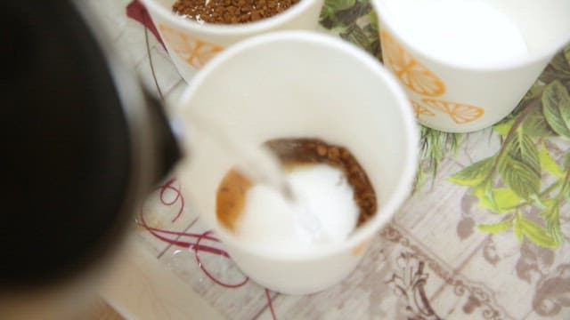 Pouring hot water into paper cups with coffee and sugar