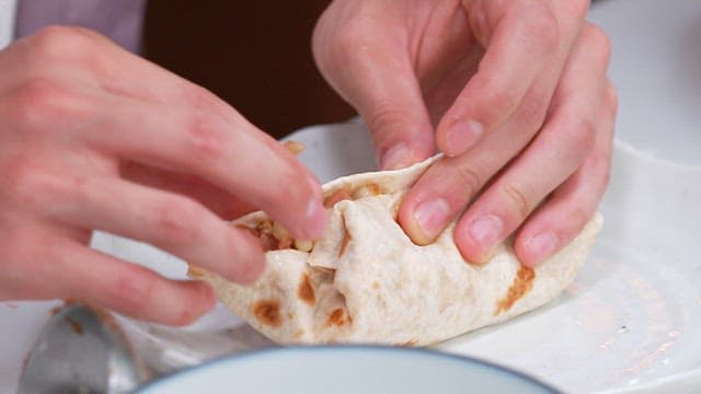 Hands Carefully Rolling up a Burrito on a pPlate