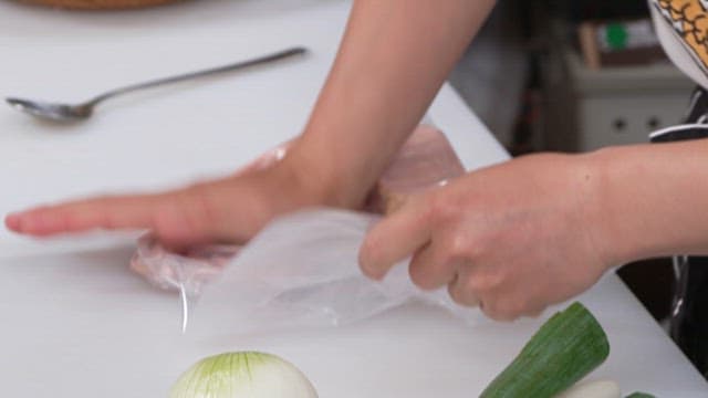 Person Crushing Ham in a Plastic Bag on a Cutting Board