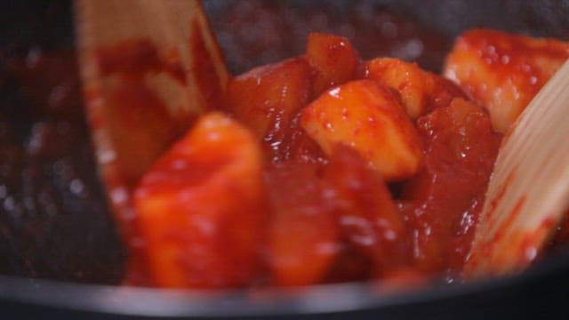Cooking spicy tteokbokki in a pan with wooden spatula