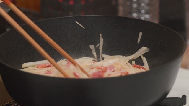 Frying shredded potato and meat in a wok with chopsticks